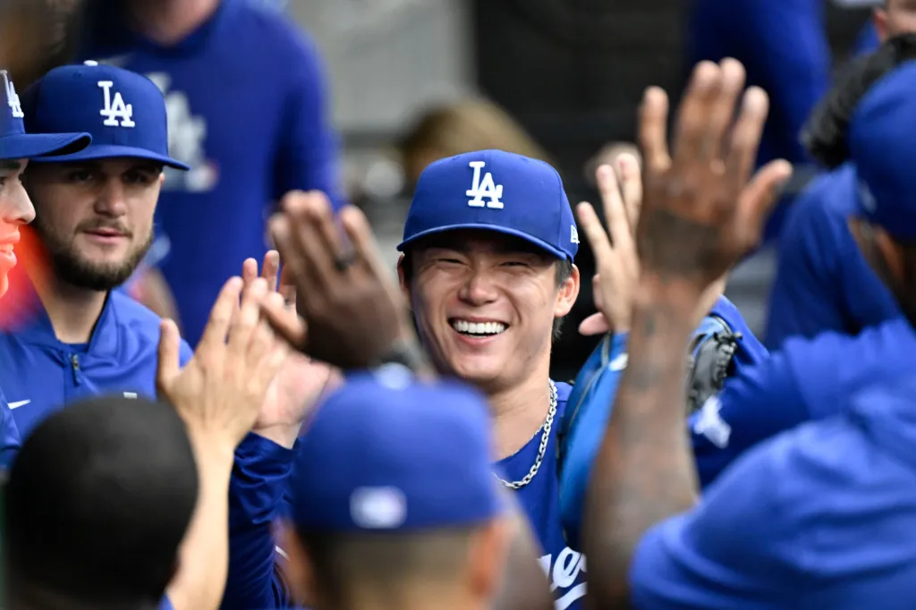 Yoshinobu Yamamoto in a blue Dodgers cap smiling, with hands in the foreground high-fiving him.