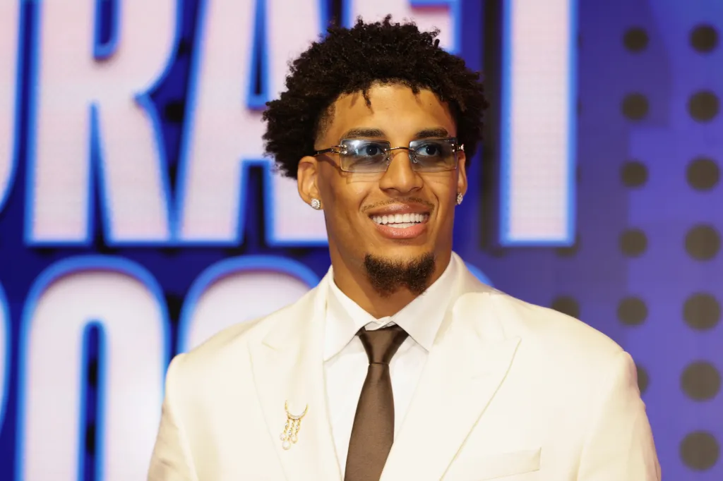 Yaxel Lendeborg in a white suit, black tie, and sunglasses with a blue background.