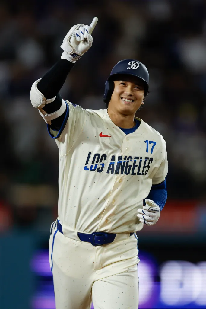 Shohei Ohtani smiling and pointing his finger in the air while wearing a Los Angeles Dodgers uniform.