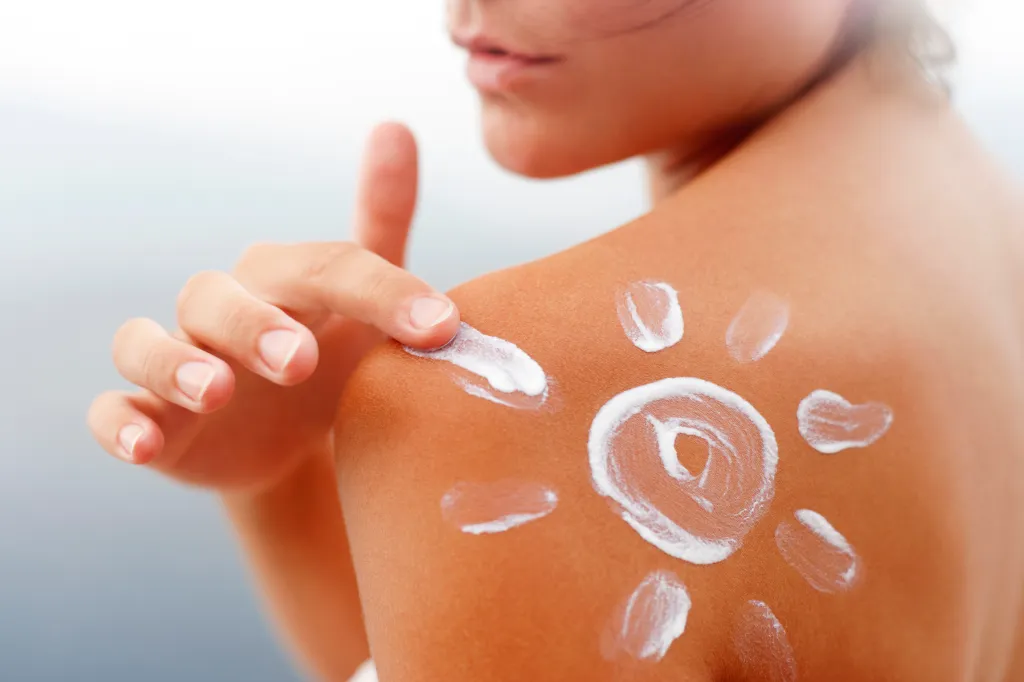 A person applies sunscreen to their tanned shoulder, forming a sun shape.