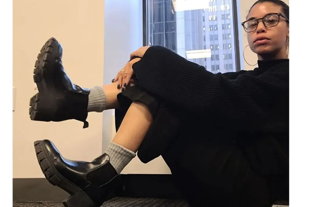 A woman wearing black boots and glasses.