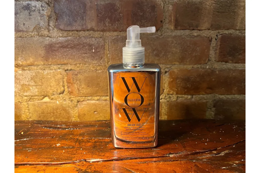 Color Wow Dream Coat Supernatural Spray on a wooden surface in front of a brick wall.
