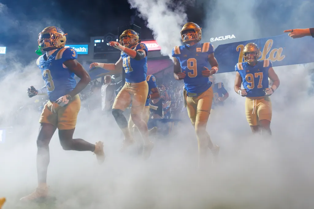 UCLA football players running out of a smoke-filled tunnel onto the field.
