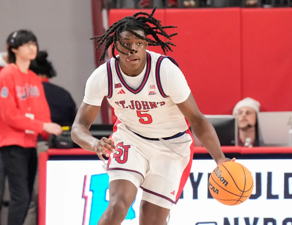 A St. John's basketball player in a white uniform dribbles the ball down the court.