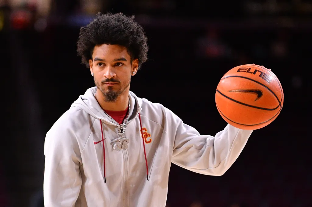 College basketball player with an afro, wearing a white USC Trojans hoodie, holding a basketball.