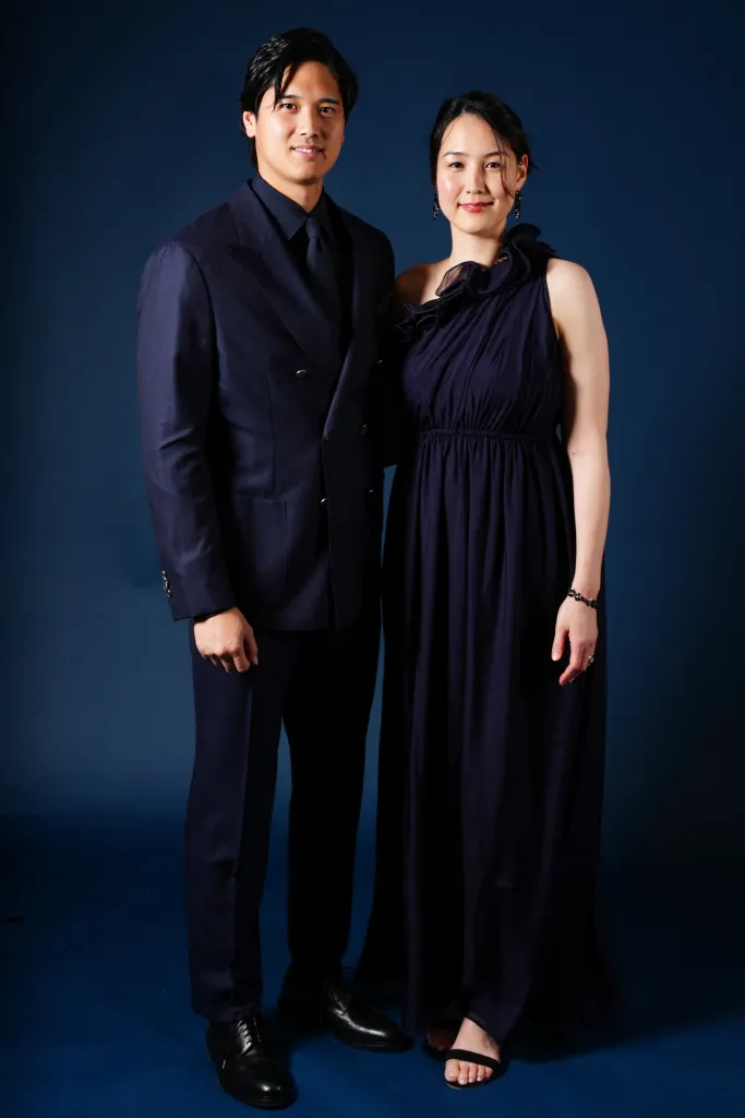A man in a navy suit and a woman in a navy ruffled gown standing together.