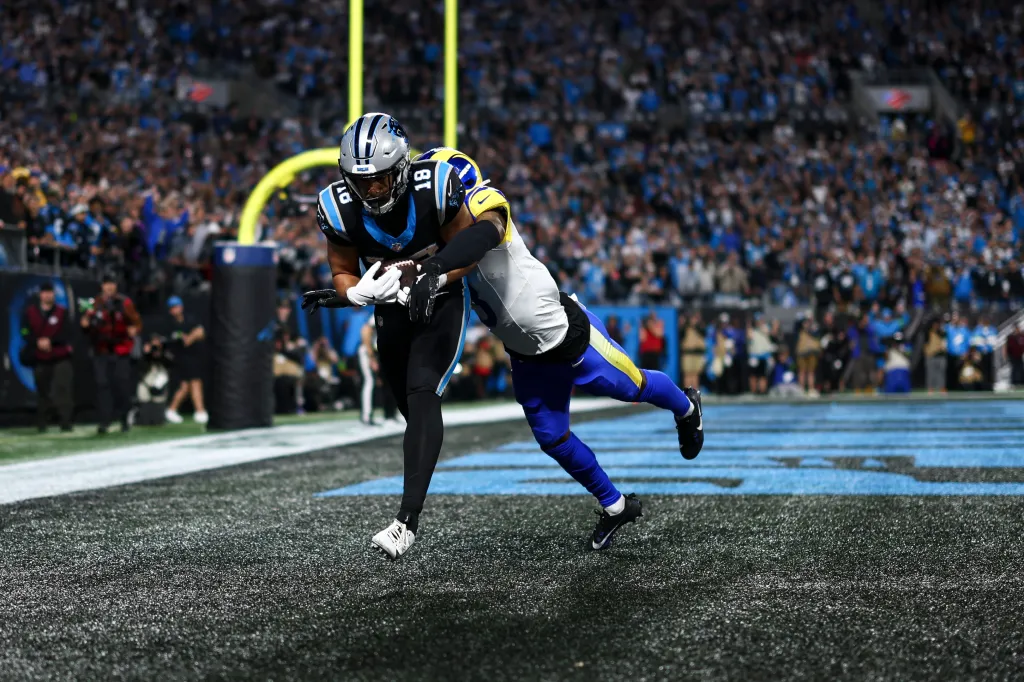 Jalen Coker #18 of the Carolina Panthers catches a pass to score a touchdown as Kam Curl #3 of the Los Angeles Rams defends during an NFL wild card playoff football game at Bank of America Stadium on January 10, 2026 in Charlotte, North Carolina.