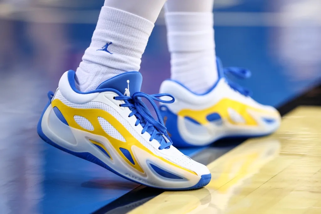 A close-up of a basketball player's white, blue, and yellow sneakers on a court.
