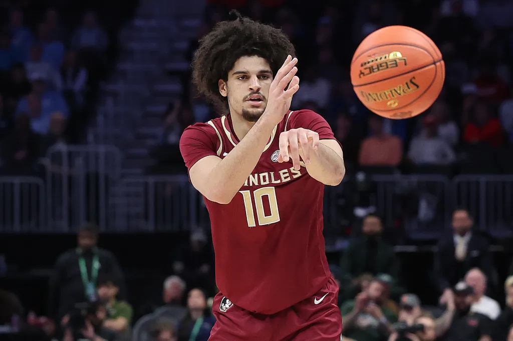 A basketball player in a maroon jersey with the number 10 reaching for a basketball.