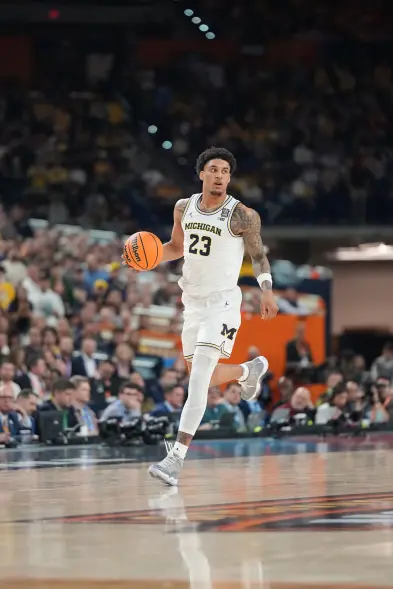Yaxel Lendeborg in a white University of Michigan basketball uniform with the number 23, dribbling a basketball on a court.