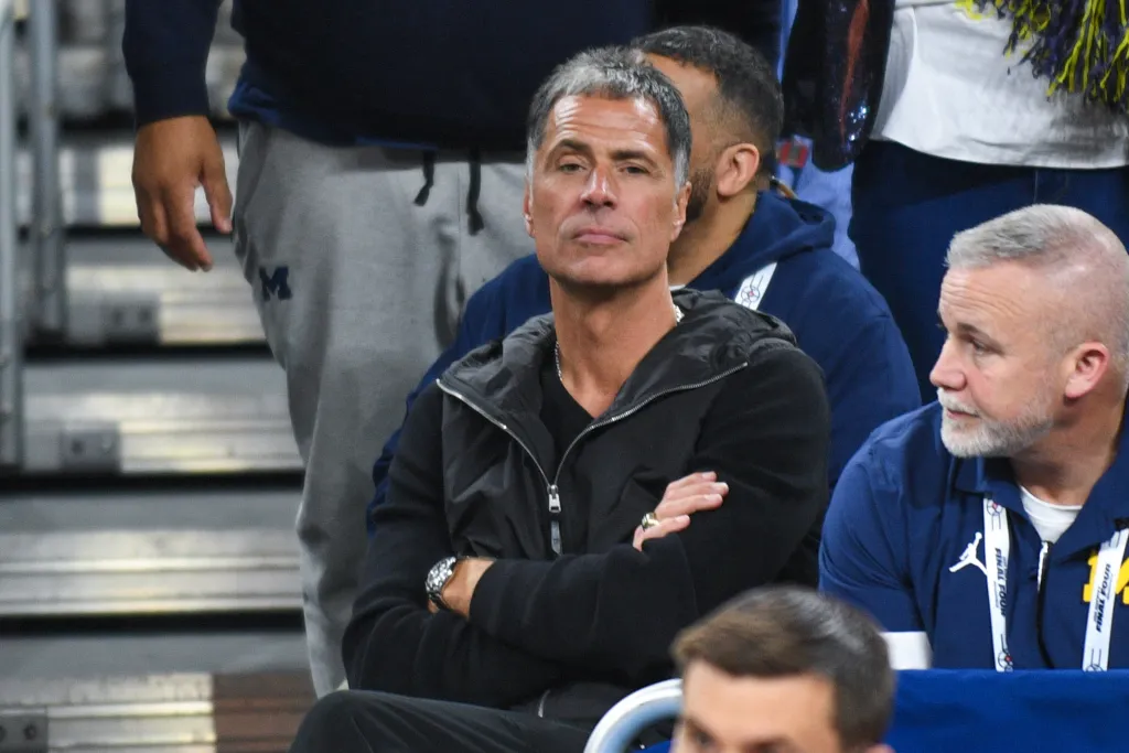 Male spectator with gray hair in a black jacket sits with his arms crossed.