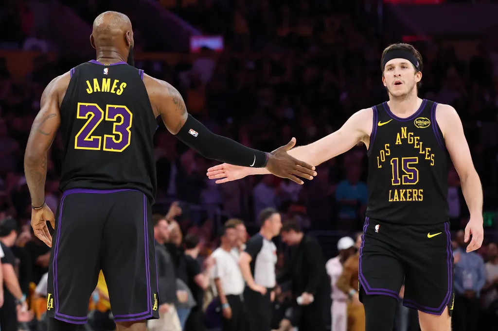 Two basketball players in black Lakers uniforms with purple and yellow accents, one with "JAMES 23" on his back and the other with "LOS ANGELES LAKERS 15" on his chest, high-five each other.