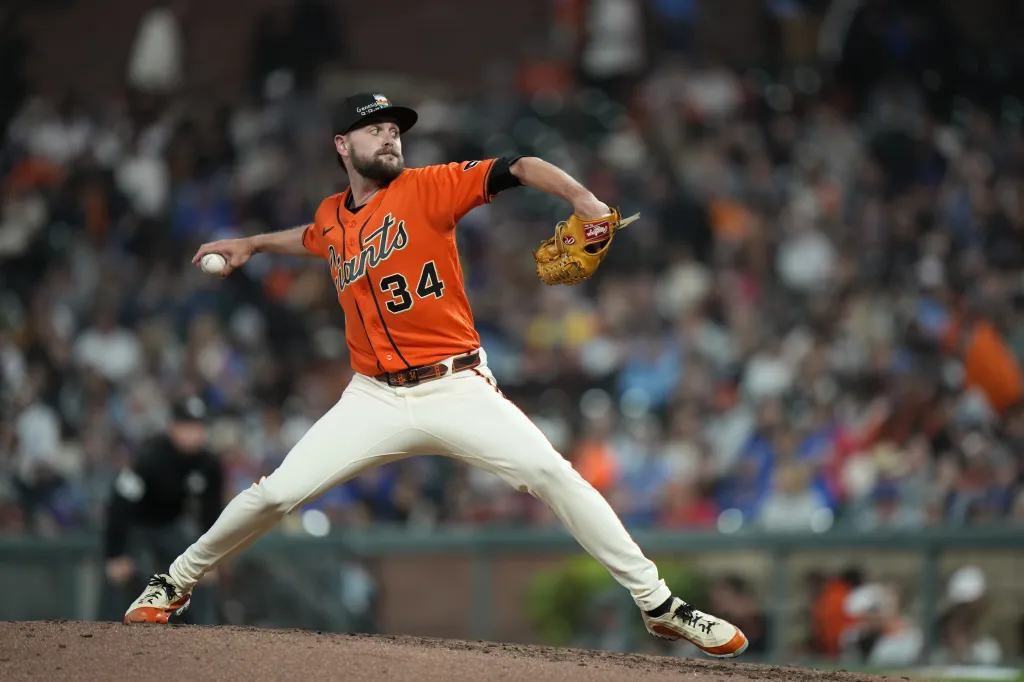 A baseball pitcher in an orange and black uniform mid-throw.