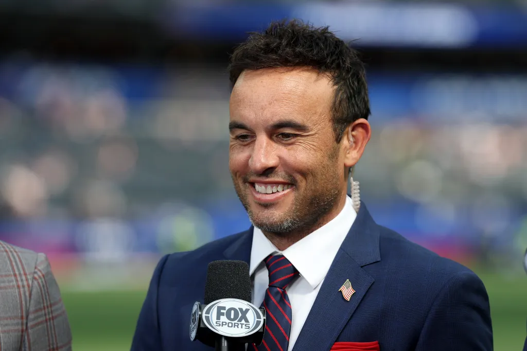 A male sports commentator smiling with a Fox Sports microphone.