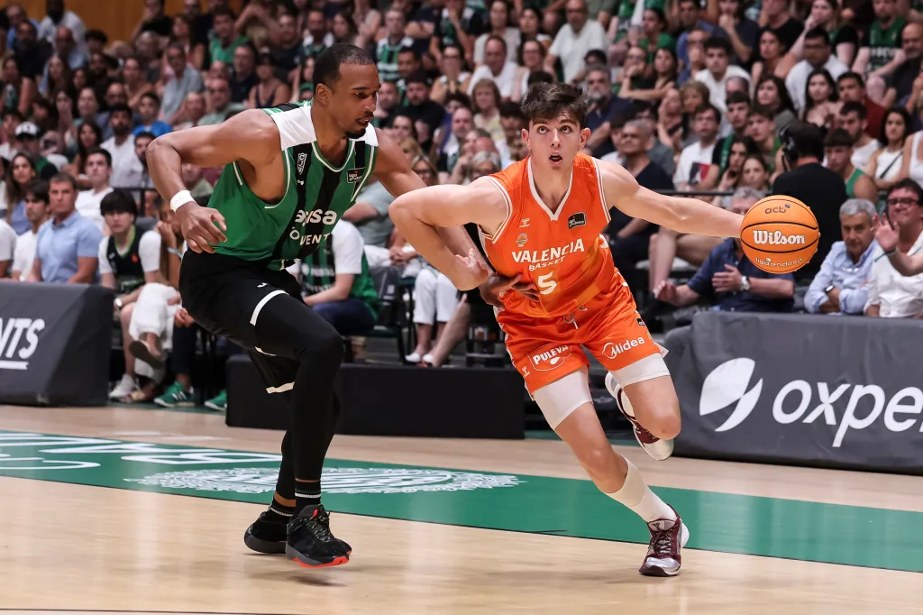 Two basketball players, one in a green and black uniform and another in an orange uniform, in action during the Asisa Joventut V Valencia Basket - Liga Acb Endesa - Semi Final Game 3.