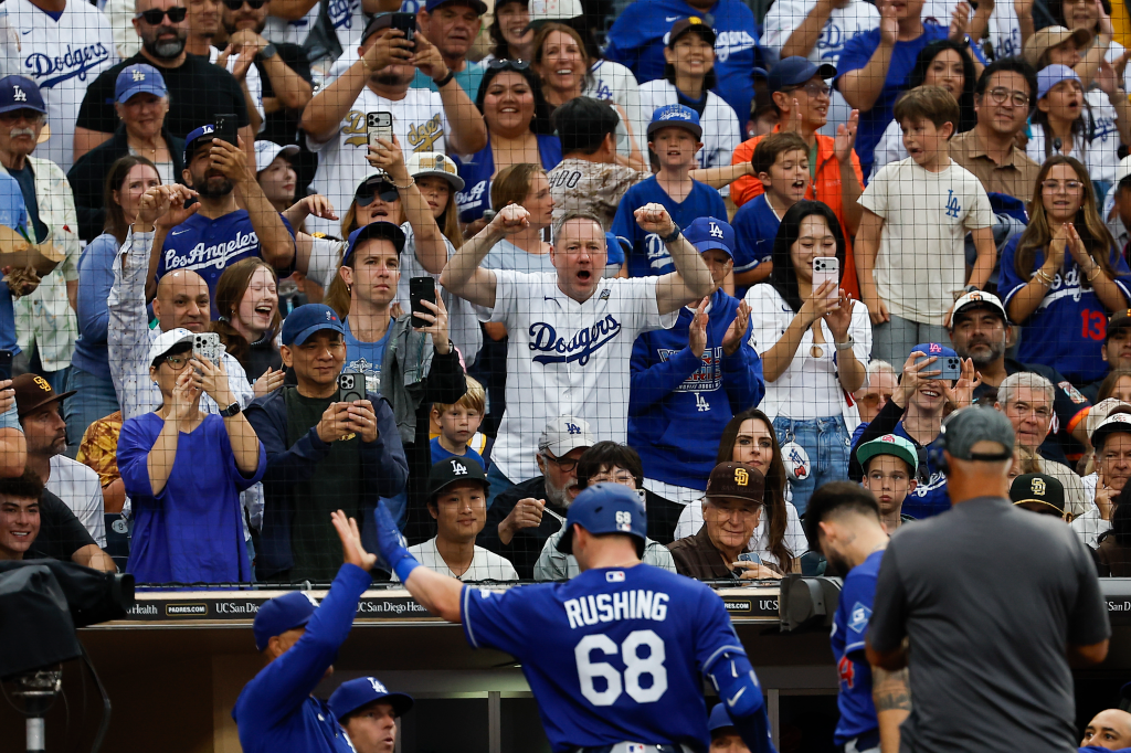Fans in the stands cheer as a Los Angeles Dodgers player high-fives a teammate in the dugout.