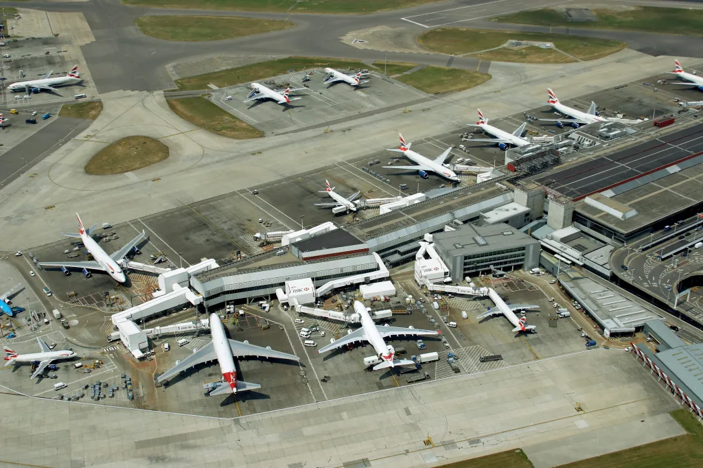Aerial view of multiple British Airways planes parked at an airport terminal with jet bridges connected.