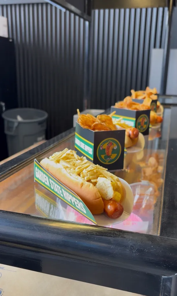Hot dogs in "Garden State Rippers" branded boxes, topped with fries or chips, on a display counter.