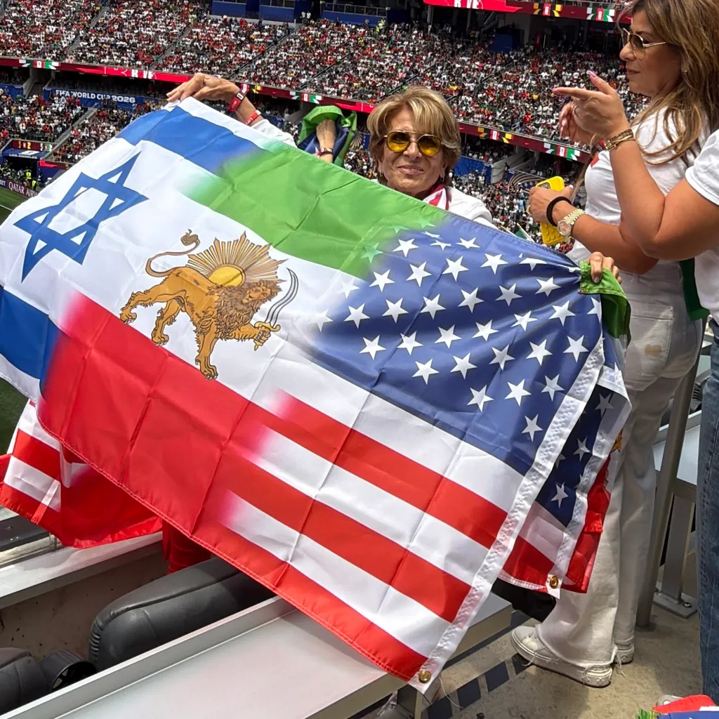 Two women at a stadium hold a flag combining the flags of Israel, Iran, and the United States.