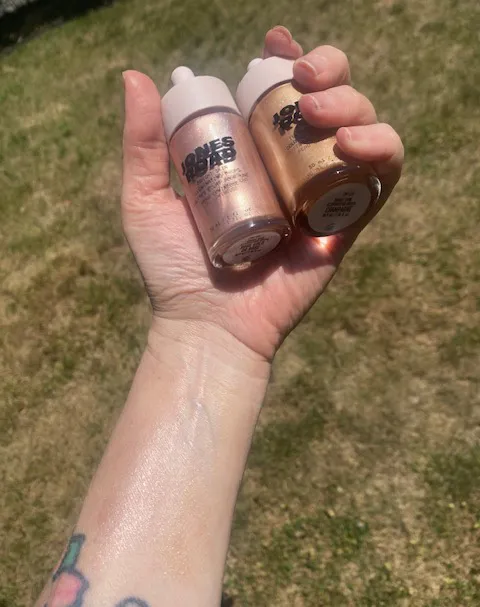 Hand holding two bottles of Jones Road skin tint, one in pink and one in gold, with the pink tint swatched on the wrist.