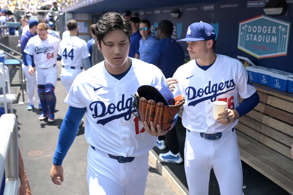 Shohei Ohtani carrying his glove and cap while walking next to another Dodgers player.