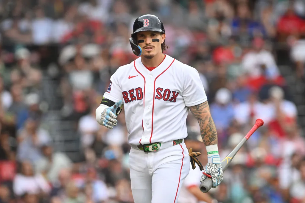 Boston Red Sox player Jarren Duran stands on the field wearing his batting helmet and holding a bat.