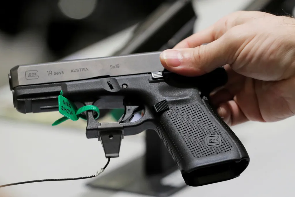 A man holding a Glock handgun with a green "NRA SHOW" tag attached to it.