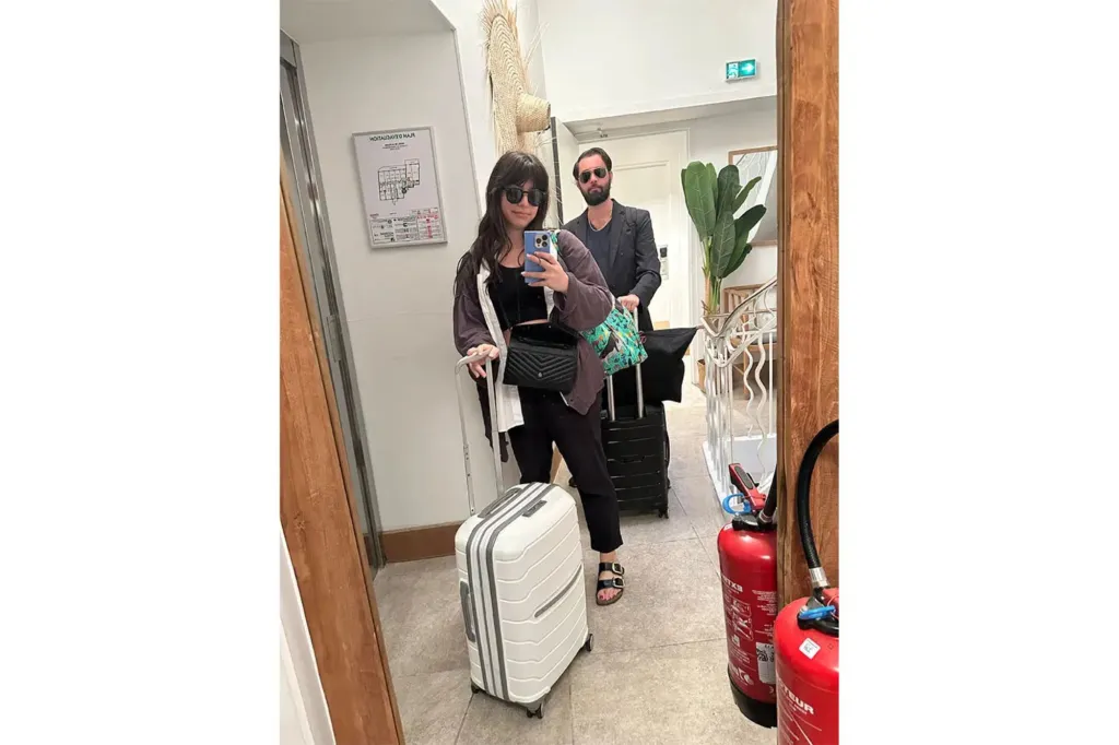 A woman taking a selfie with her suitcase, and husband.