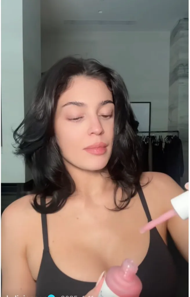 A woman in a black top holding a dropper bottle of pink liquid.