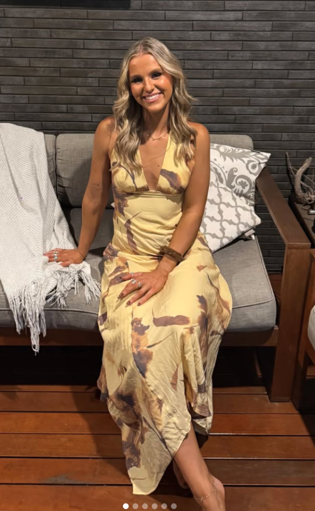 A woman with blonde hair wearing a patterned yellow dress sits on an outdoor couch.