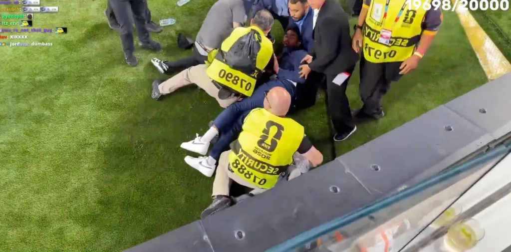 Security personnel apprehending a man in a blue suit on a grassy field.