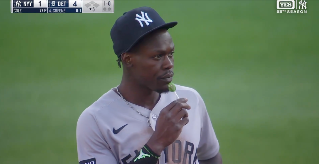 Baseball player in a New York Yankees uniform and cap eating a green lollipop.