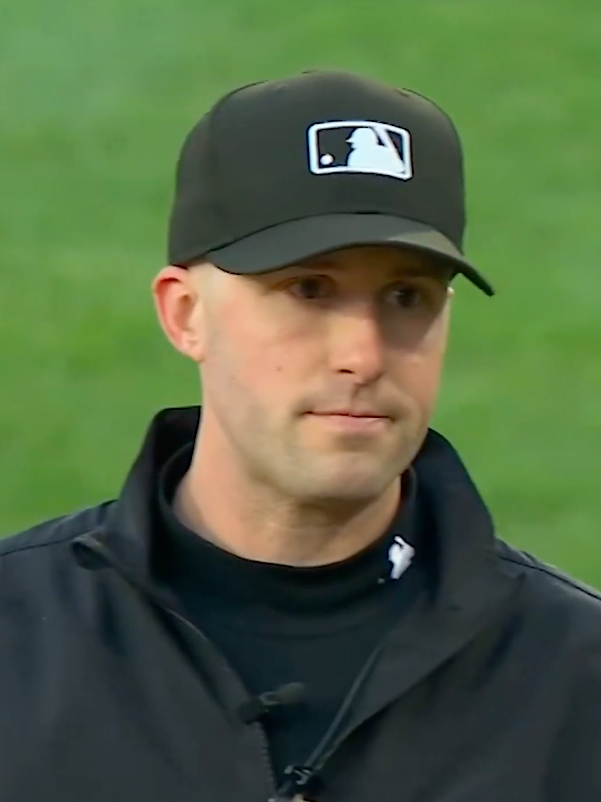 A male baseball umpire wearing a black MLB cap and black jacket.