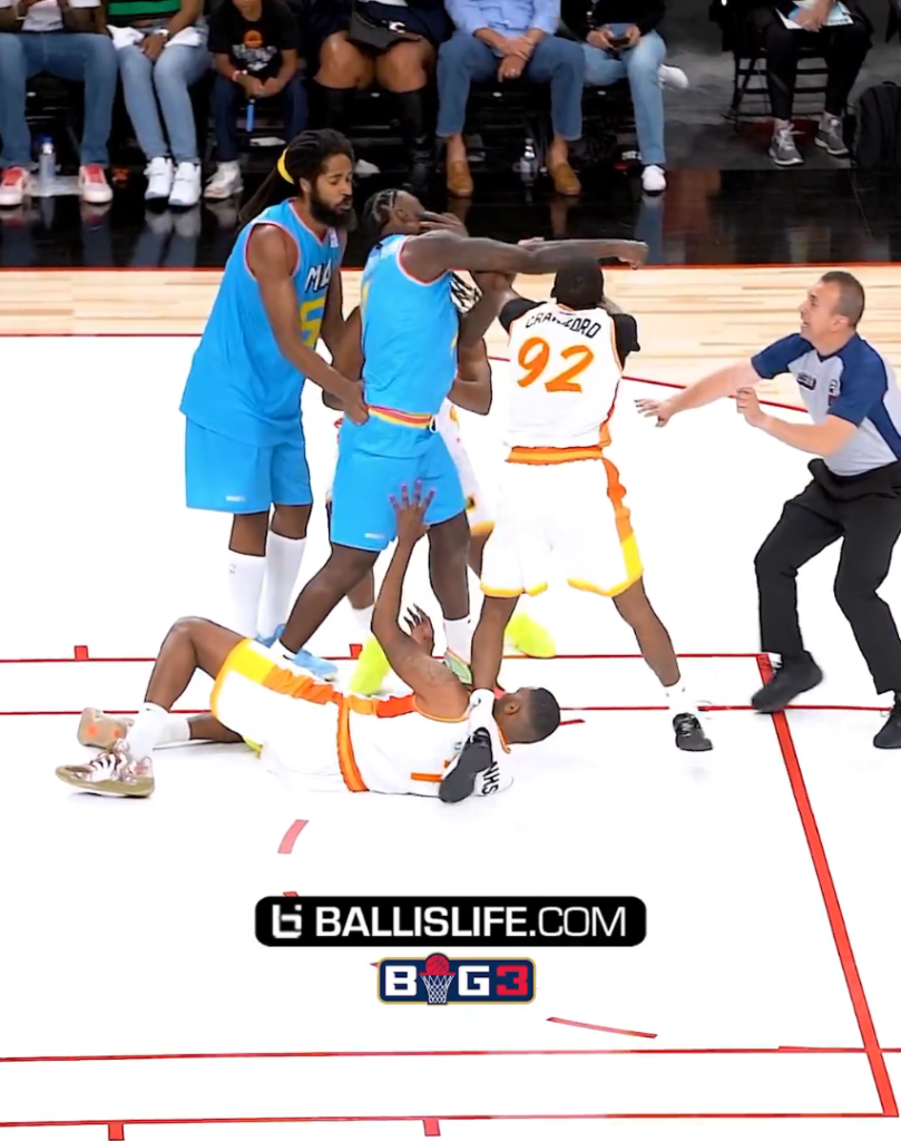 Basketball players in blue and white jerseys in an altercation, with a referee trying to intervene.
