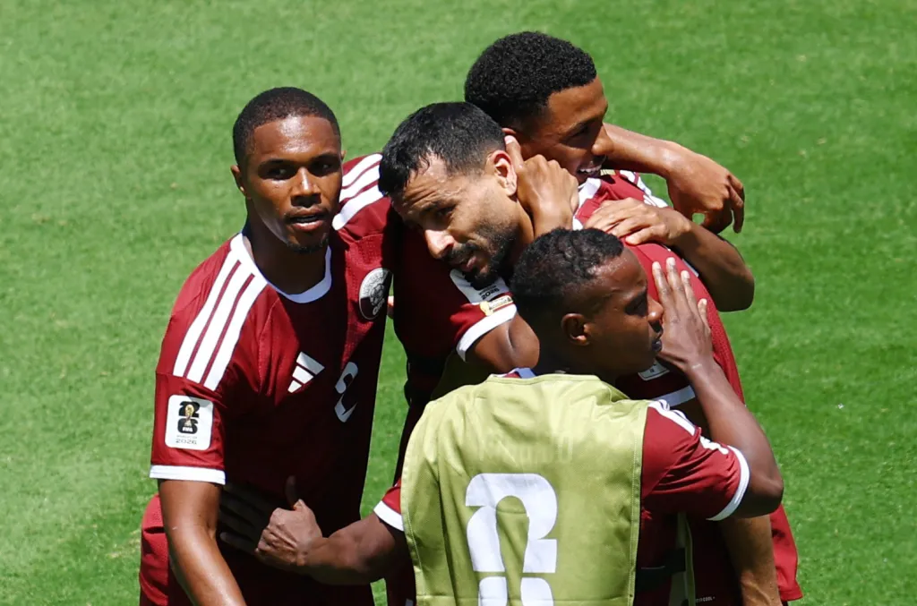 Four soccer players from Qatar celebrate a goal during a FIFA World Cup 2026 match against Switzerland.