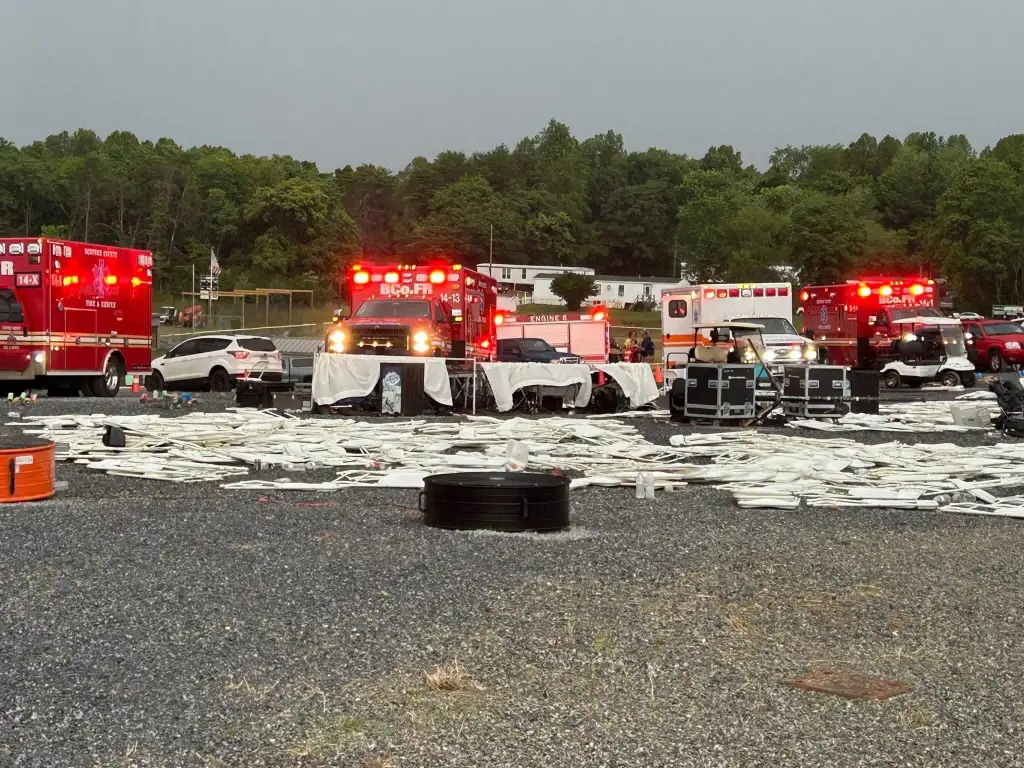 Multiple emergency vehicles, including fire trucks and ambulances, gathered in a gravel lot surrounded by trees.