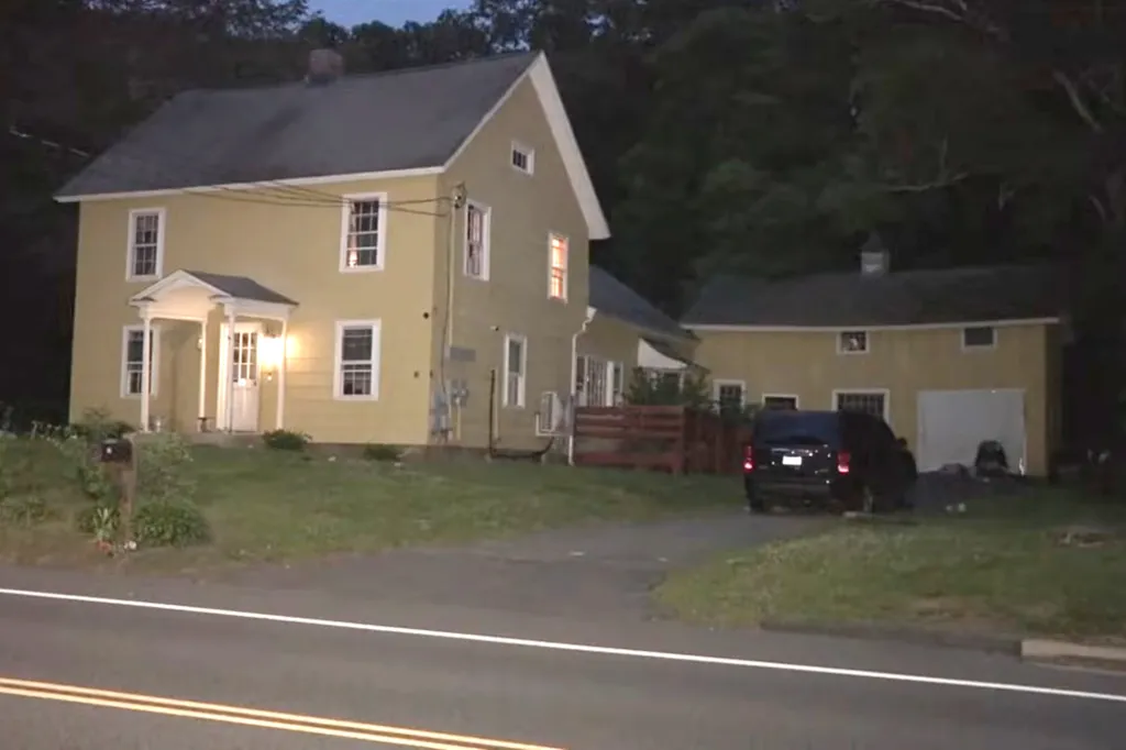 Exterior of a two-story yellow house and an attached smaller yellow building at dusk, with a dark SUV parked in the driveway.