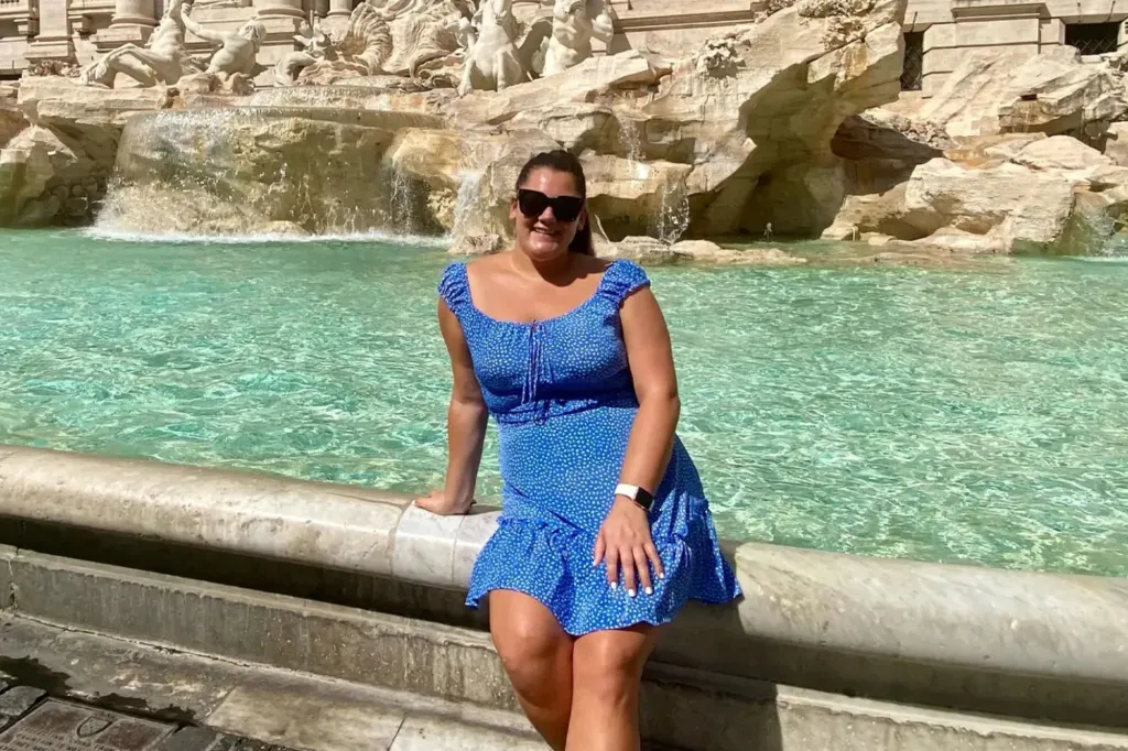 A woman in a blue mini dress sitting by a fountain.