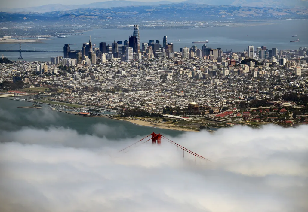 Aerial view of the Golden Gate Bridge shrouded in fog, with the San Francisco skyline and bay in the background.
