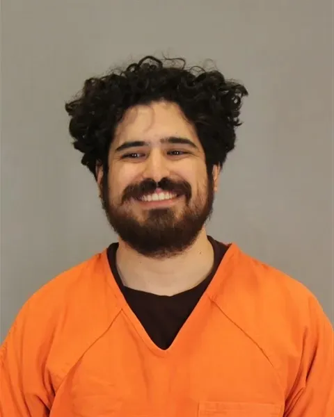 Mugshot of Abraham Alvarez, a smiling man with dark curly hair and a beard, wearing an orange jumpsuit.