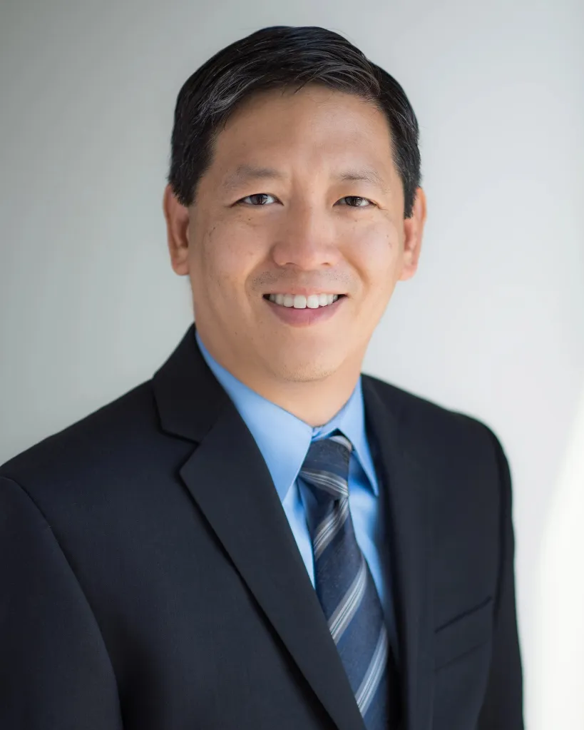 Felix Fang smiling, wearing a dark suit and striped tie.