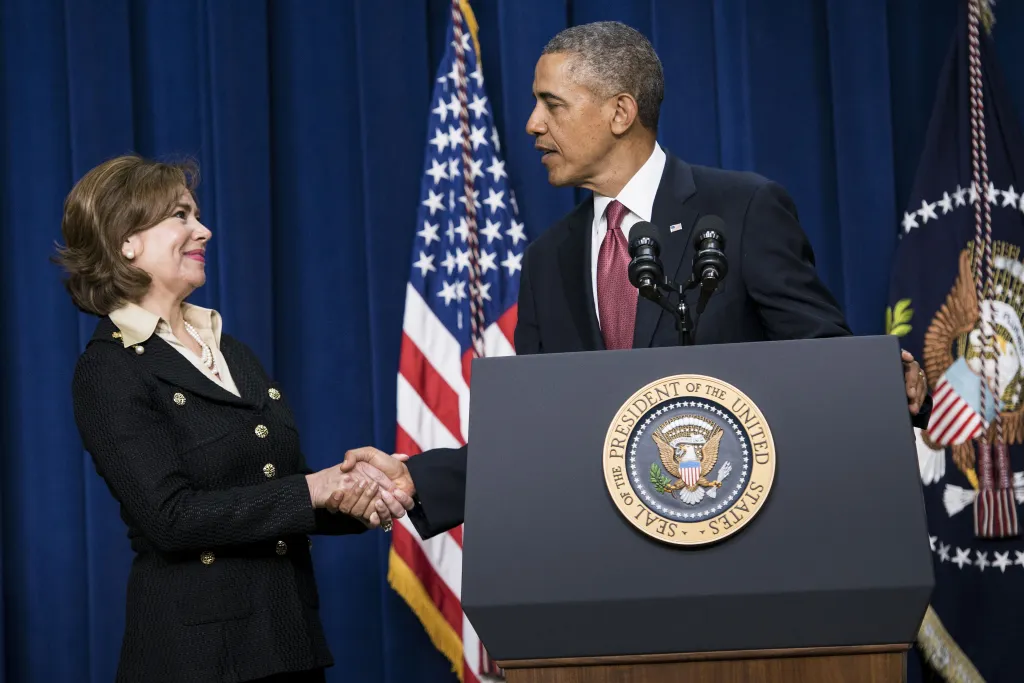Maria Contreras-Sweet shaking hands with Barack Obama at a podium with the Seal of the President.