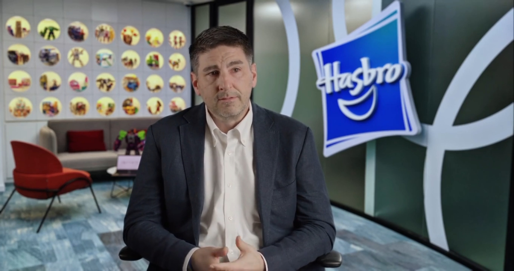 Matt Proulx at the Milken Institute, with a Hasbro logo and branded wall behind him.