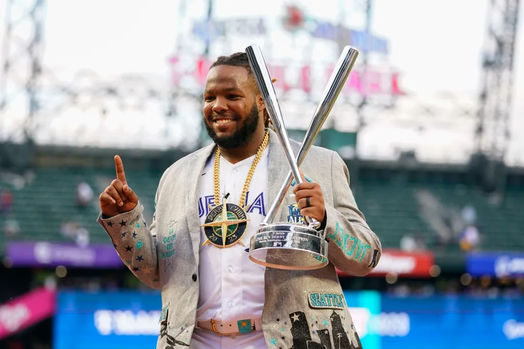 Vladimir Guerrero Jr. smiling while holding his Home Run Derby trophy and pointing upwards.