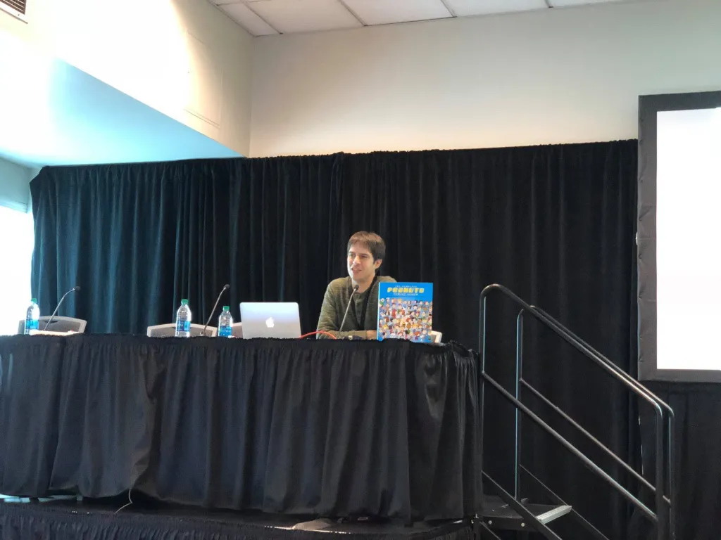 Andrew Farago seated at a table with a laptop and a "Peanuts" book.
