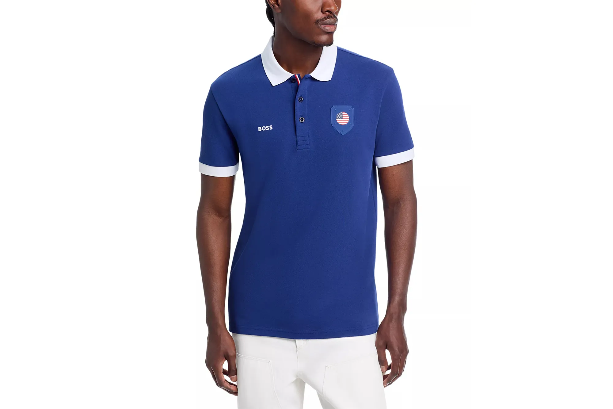 Model wearing a blue BOSS polo shirt with white trim on the collar and sleeves, and a patch featuring a US flag on the chest.