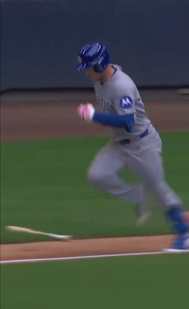 A baseball player in a blue helmet and gray uniform running, with a baseball bat lying on the ground behind him.