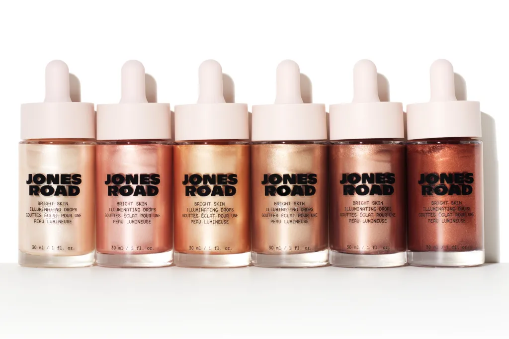 Six bottles of Jones Road Bright Skin Illuminating Drops in varying shades, from light to dark.