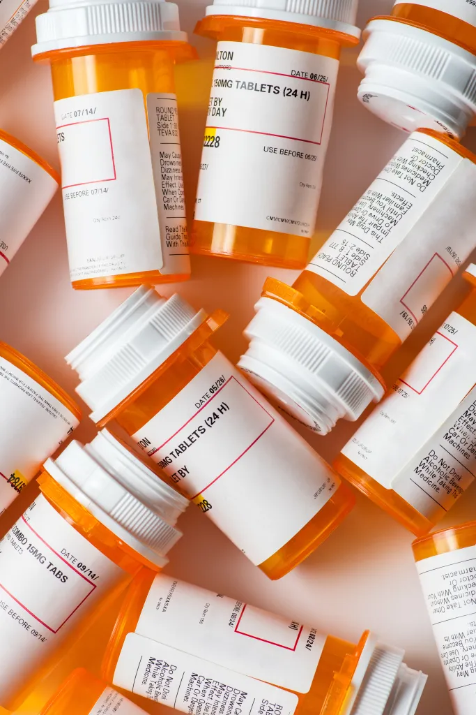 A group of prescription pill bottles with visible labels and warnings scattered on a white background.