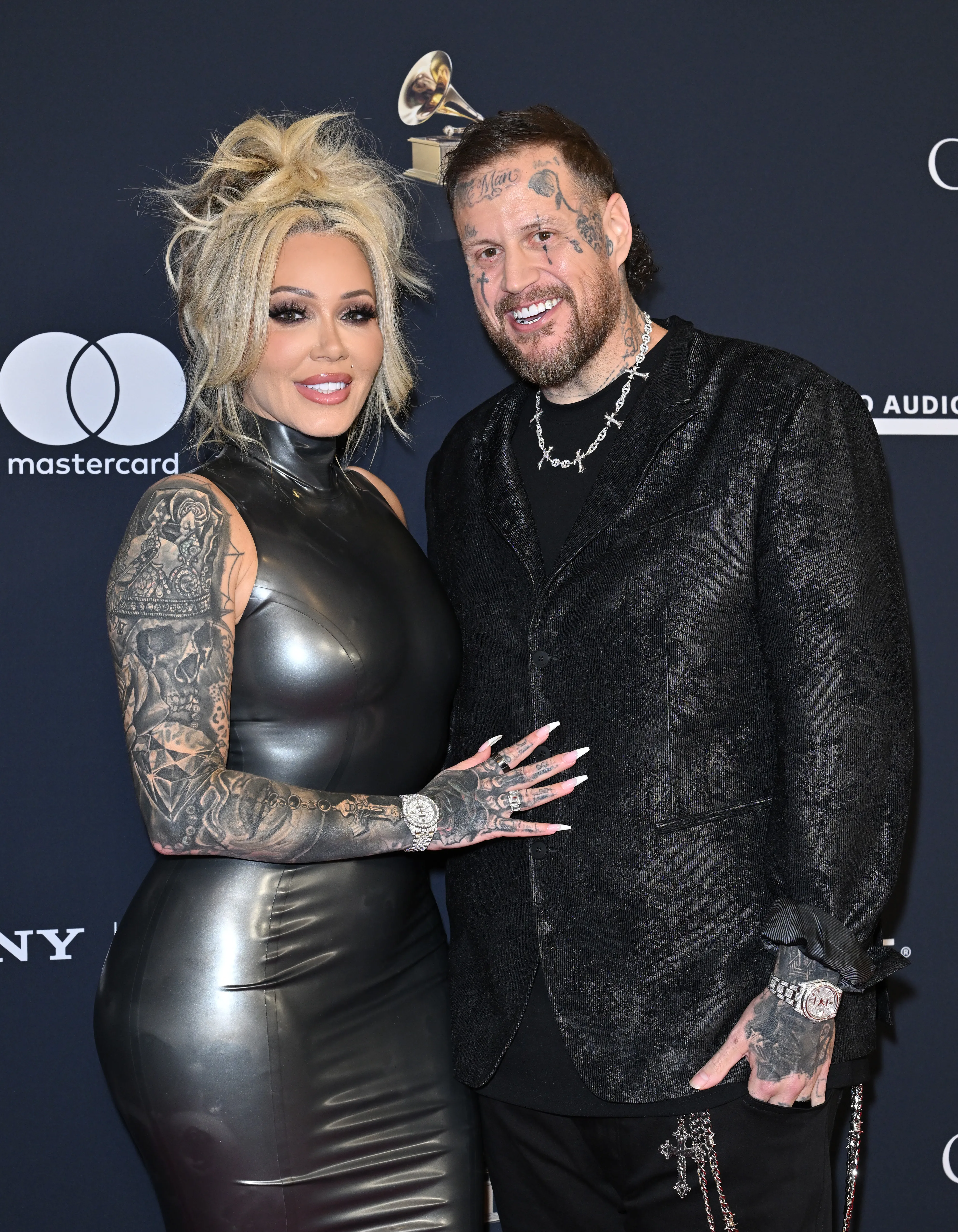 Bunnie Xo, in a black latex dress, and Jelly Roll, in a black suit with face and arm tattoos, pose together at the 68th GRAMMY Awards Pre-GRAMMY Gala.